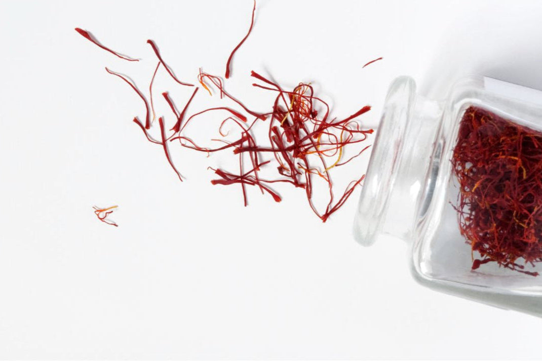 Saffron threads spilling out of a glass container on a white background